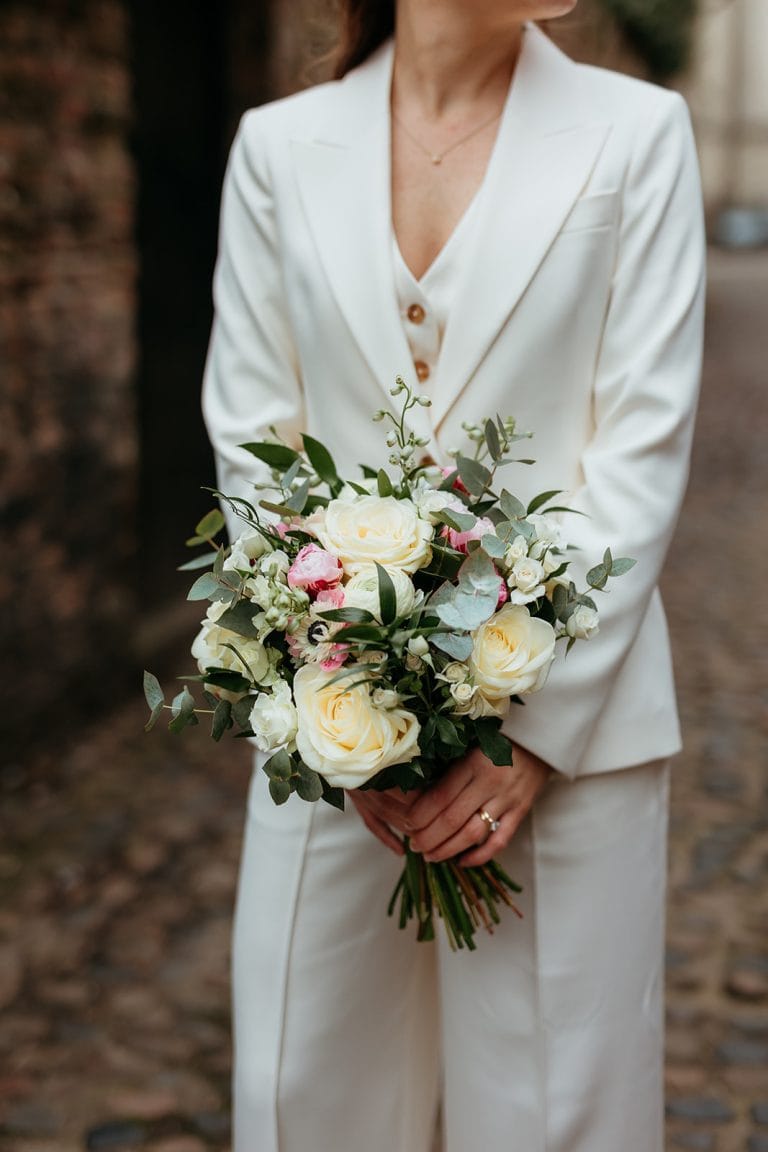 Bride in white suit holding a beautiful wedding bouquet outdoors.