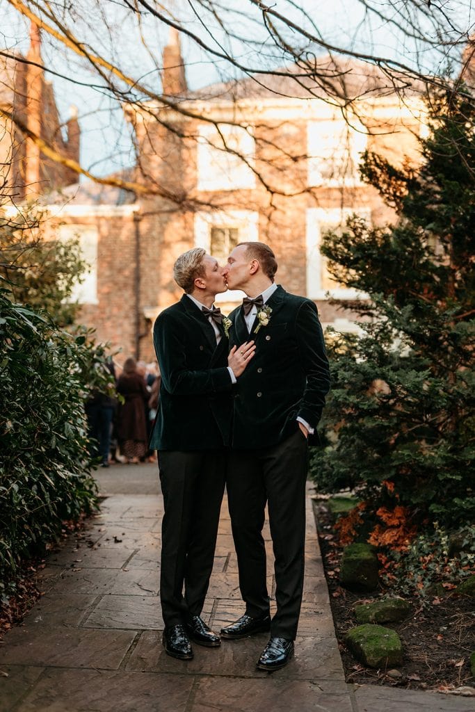 Intimate kiss between wedding couple in York Register Office gardens with guests in background