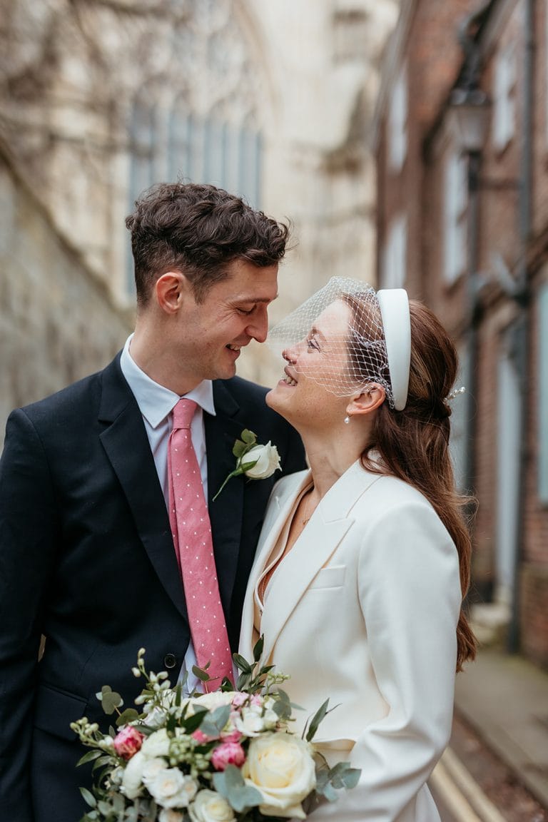 Happy wedding couple in stylish attire in city alleyway.