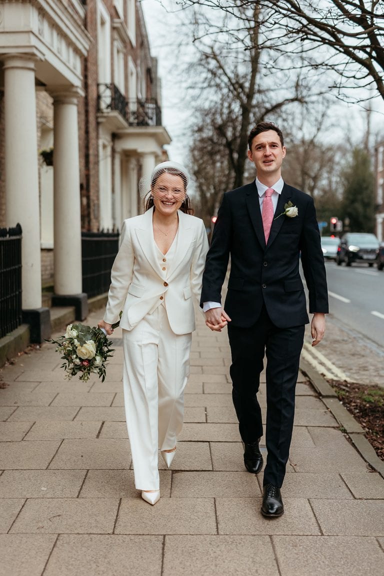Happy wedding couple walking hand in hand on city sidewalk.
